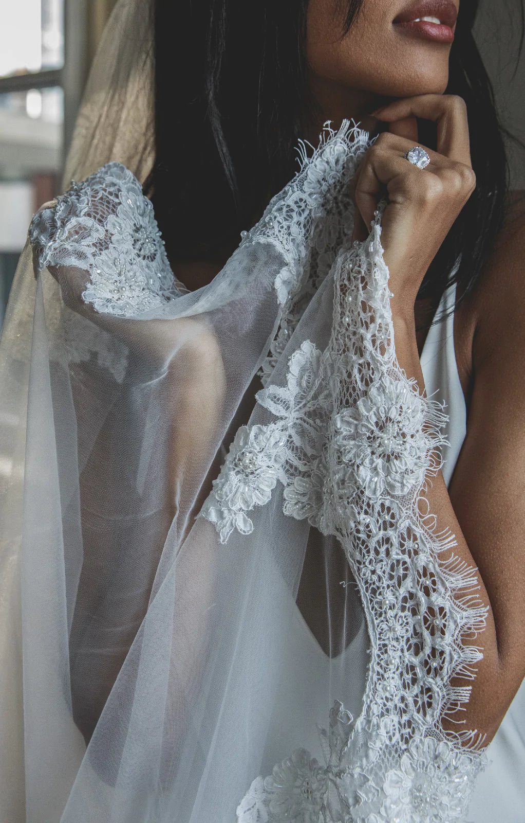 Close-up of Jamie wedding veil showing scalloped Chantilly lace edge with beaded floral appliqué held by model