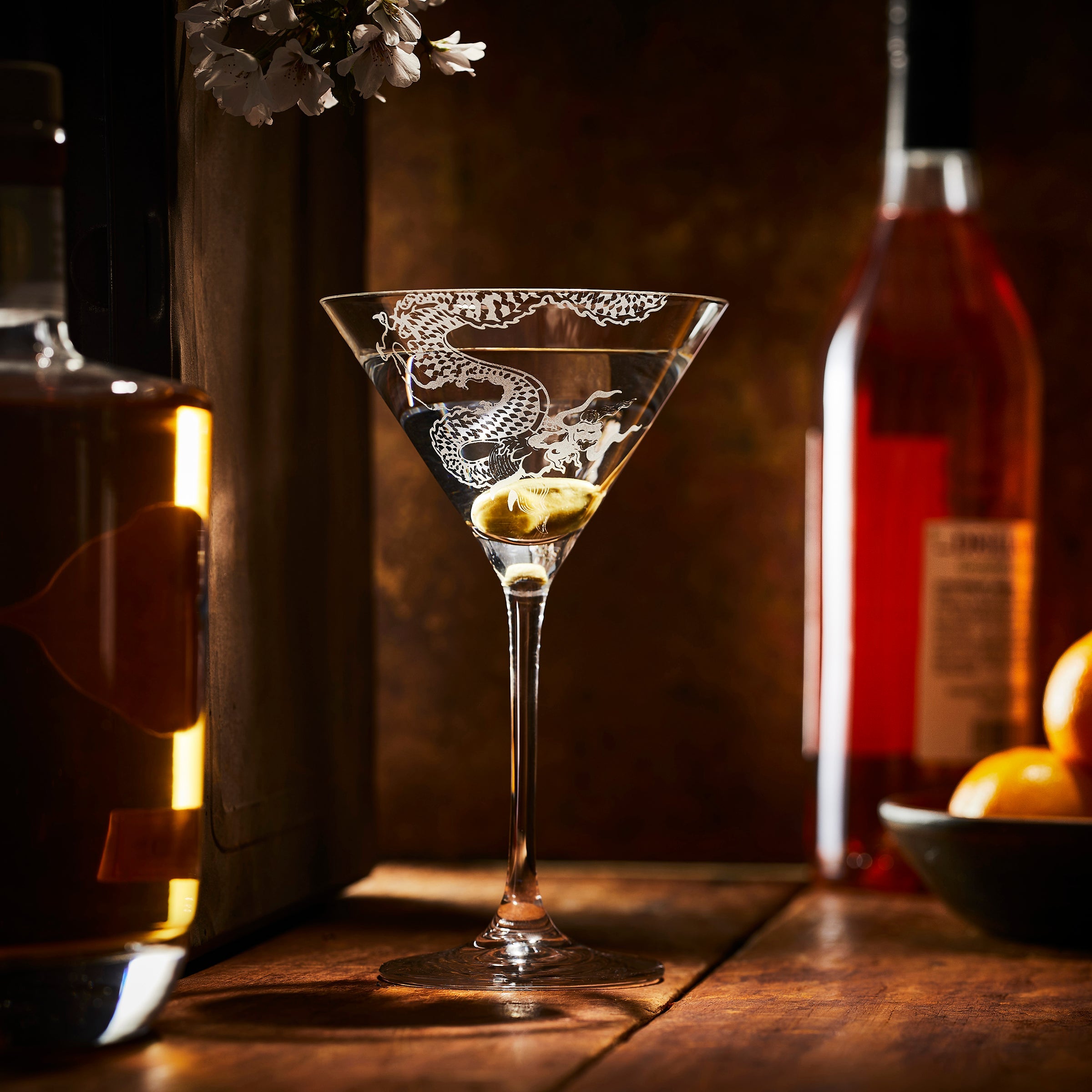 Etched Crystal Dragon Martini glass with a martini and an olive on a bar from Caskata