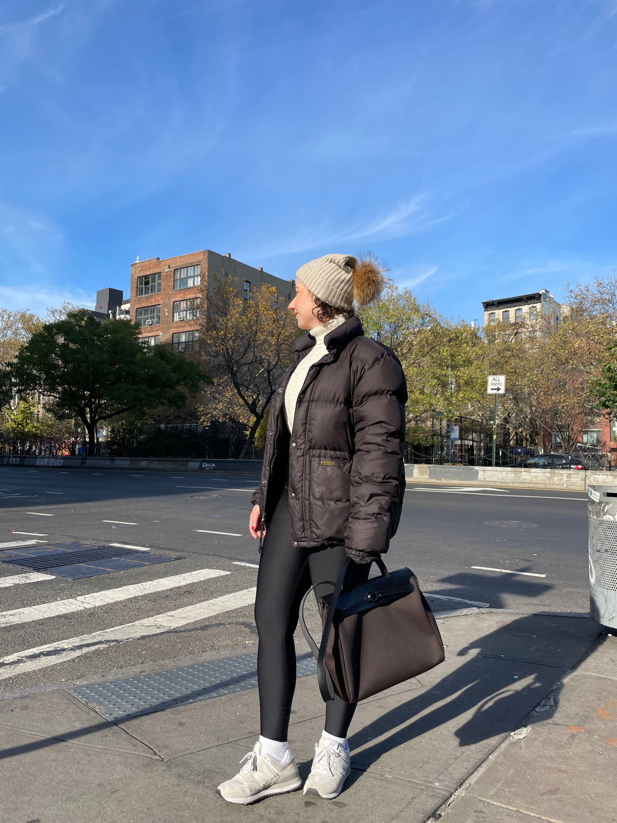 Woman wearing the beige striped cashmere pom beanie while walking on a city street