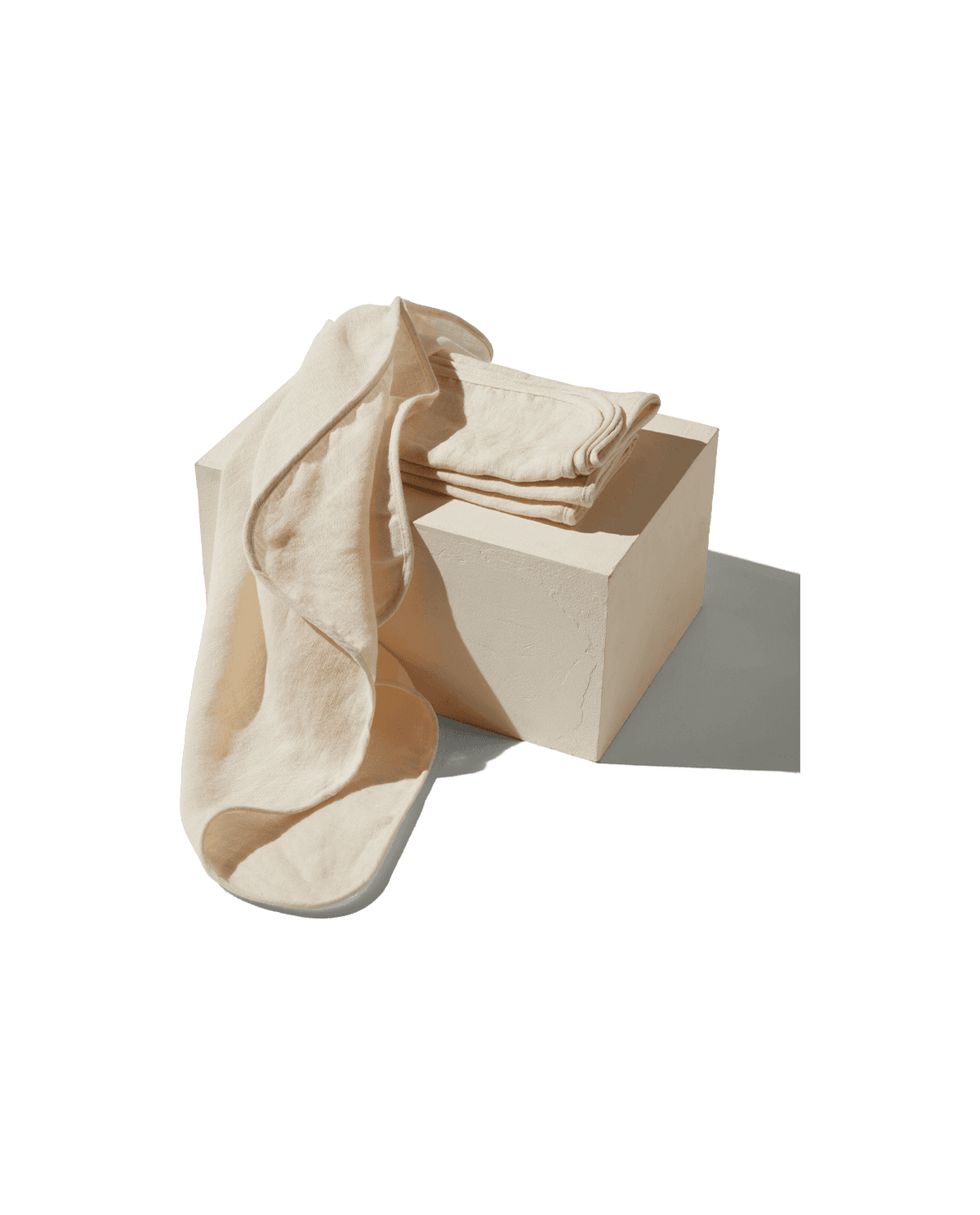 Angled view of The Linen Napkins, Set of 4 showcasing stonewashed 100% flax linen with folded napkins on a cream block
