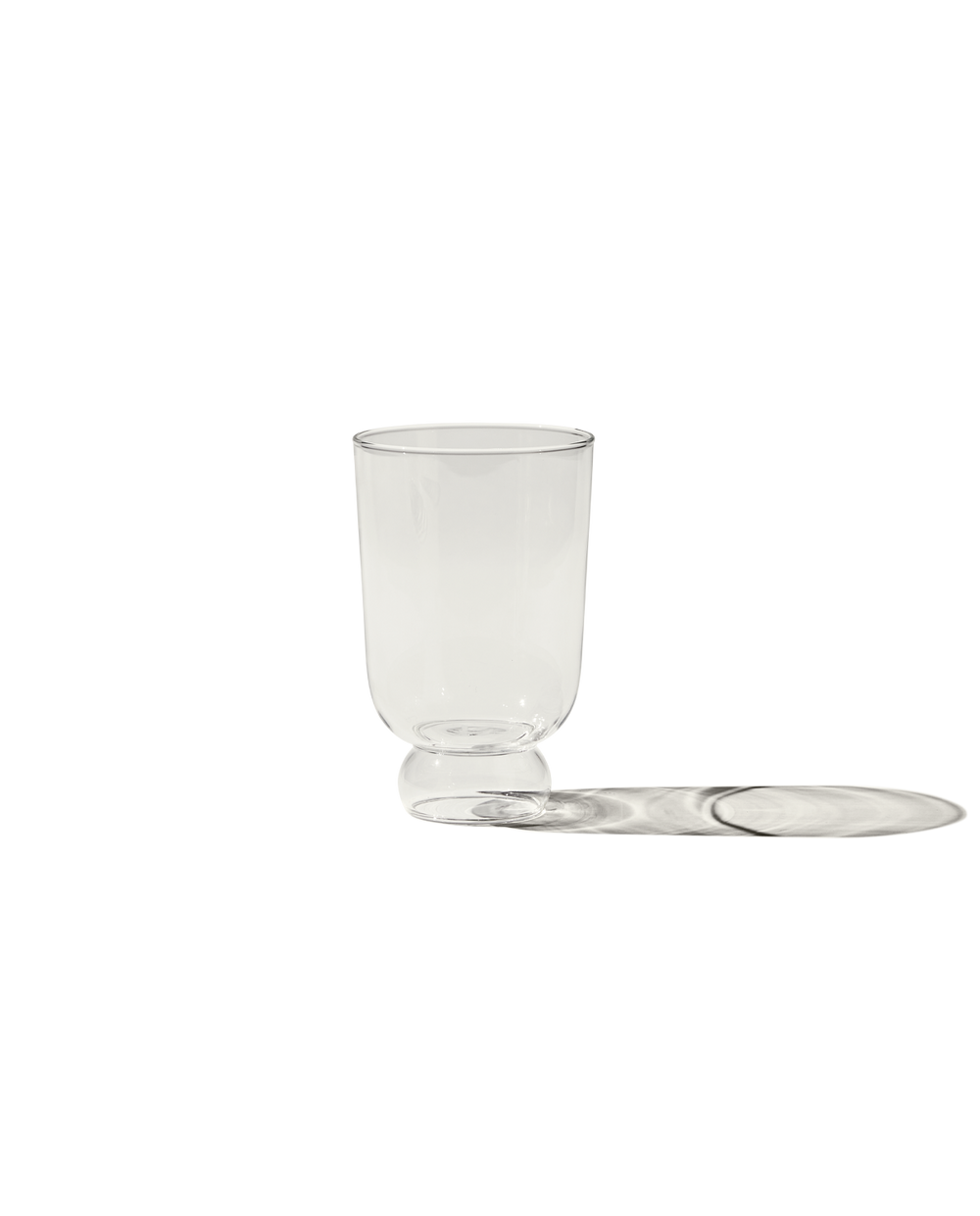 Front view of The Full Glass clear drinking glass with short rounded pedestal base on black background casting a long shadow