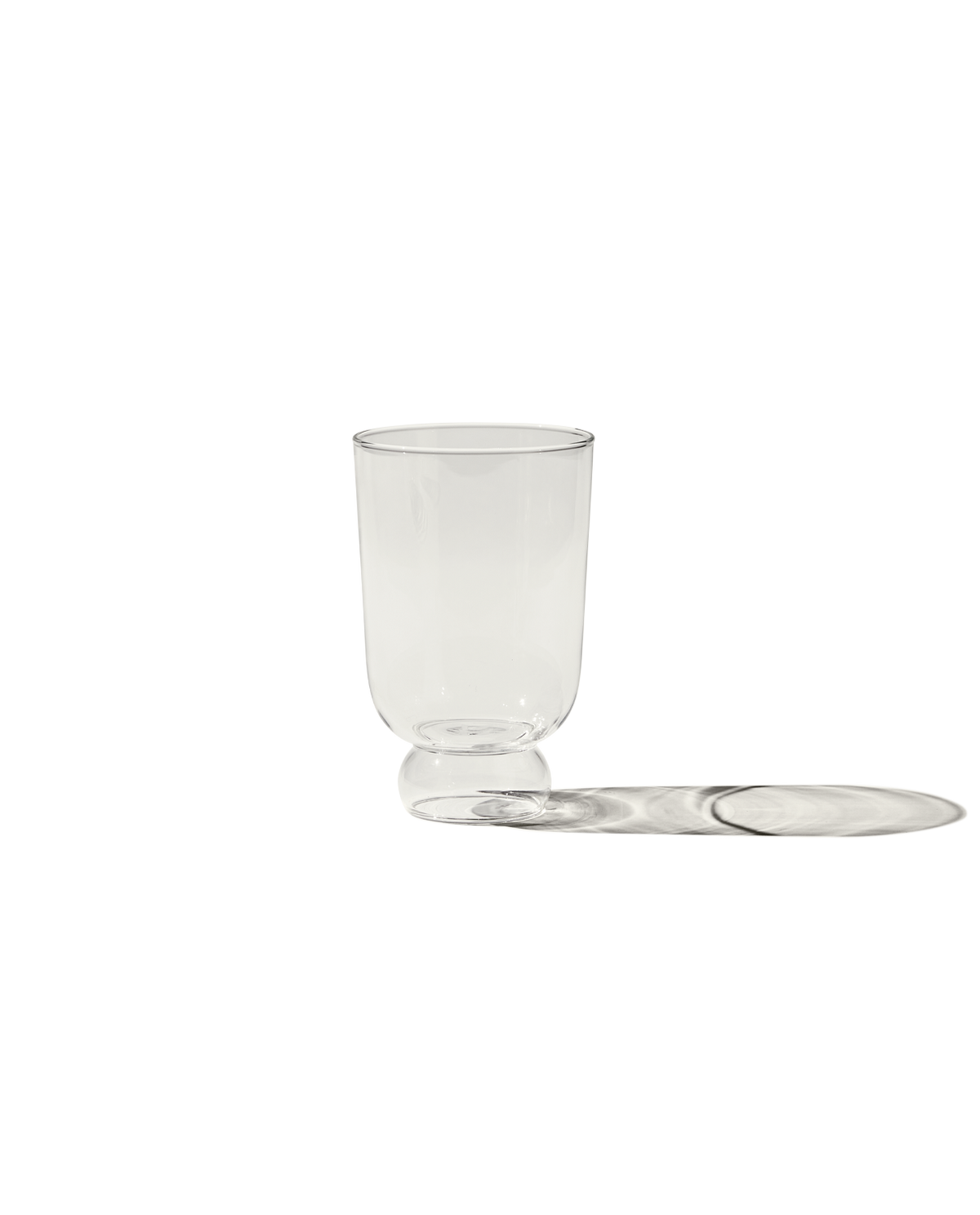 Front view of The Full Glass clear drinking glass with short rounded pedestal base on black background casting a long shadow