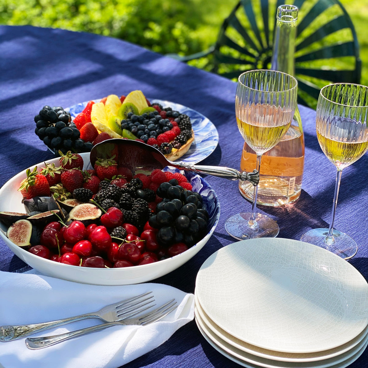 A table with a Peony Blue Wide Serving Bowl of fruit and a glass of wine from Caskata Artisanal Home.