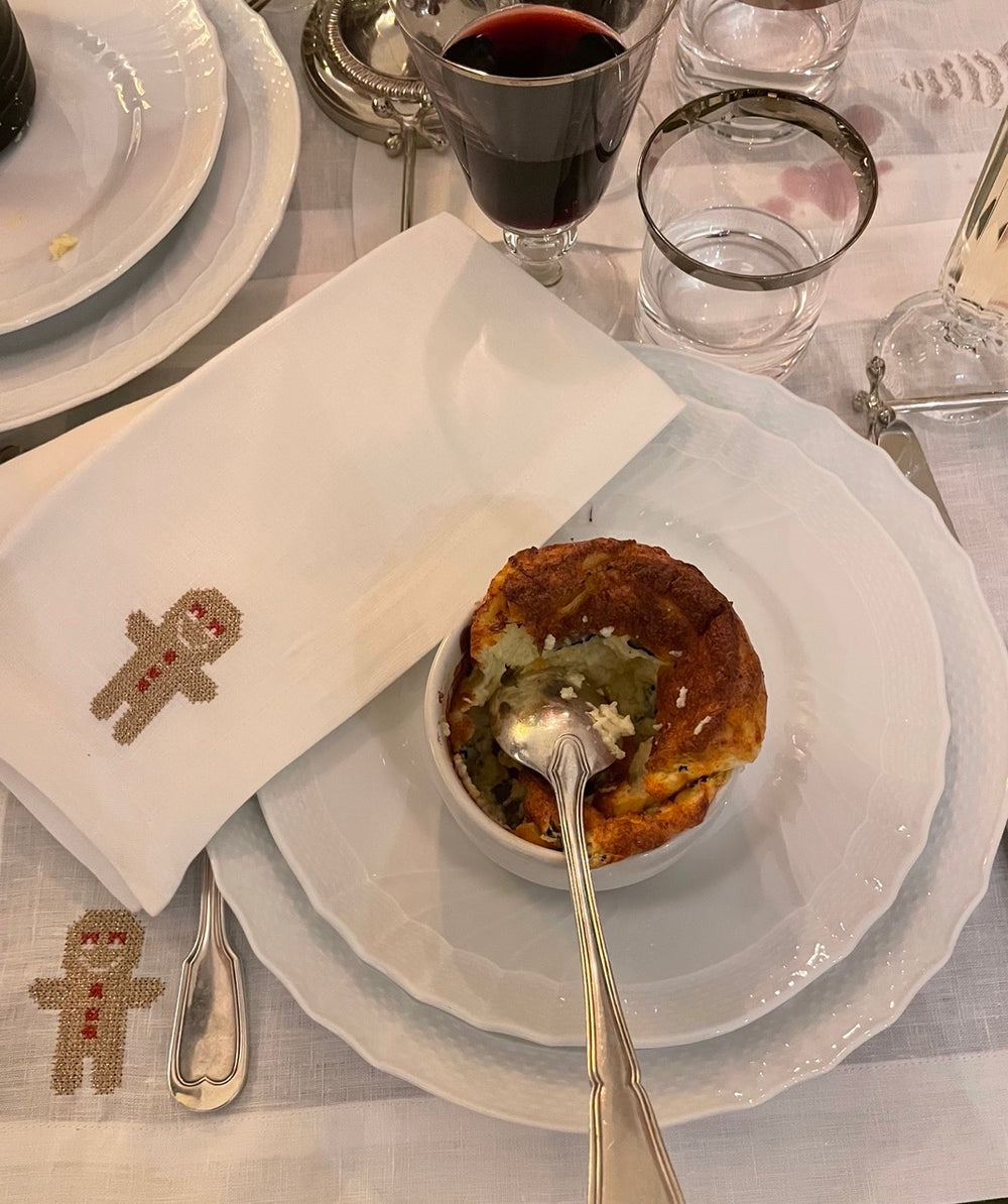 Folded white linen napkin, set of 4, embroidered with gingerbread man next to layered white plates and ramekin
