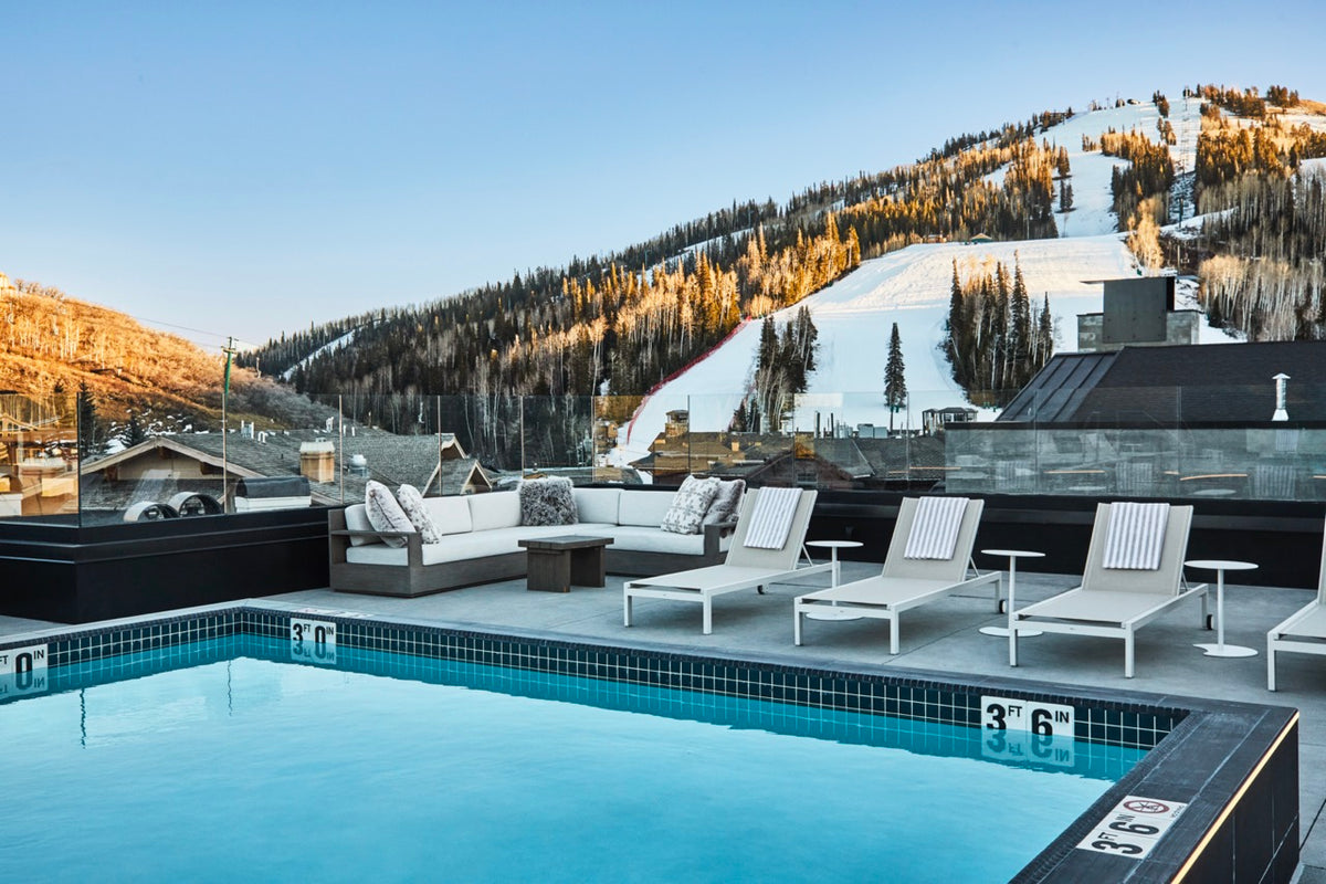 Rooftop pool and lounge seating overlooking snow-covered ski slopes and mountain at sunset