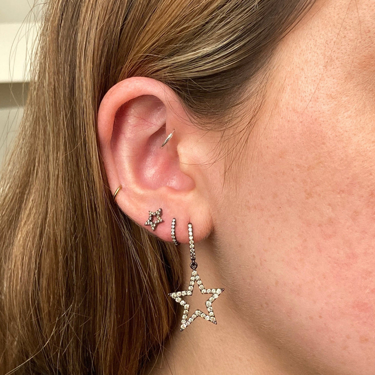 Close up side view of Huggie Hoops pair on model ear showcasing dangling star and pave crystals against neutral background