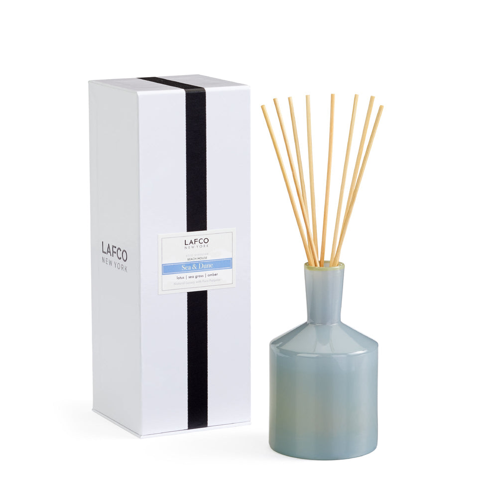 Front view of Sea & Dune reed diffuser showing pale blue glass vessel with natural rattan reeds and white gift box on white background