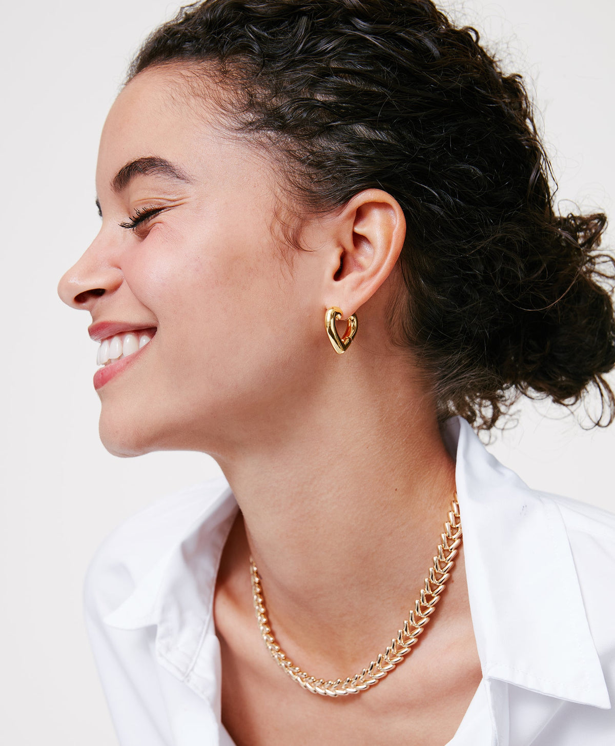 Profile view of The Heart Chubbies gold-tone heart hoop earrings on model, chunky polished finish, neutral background