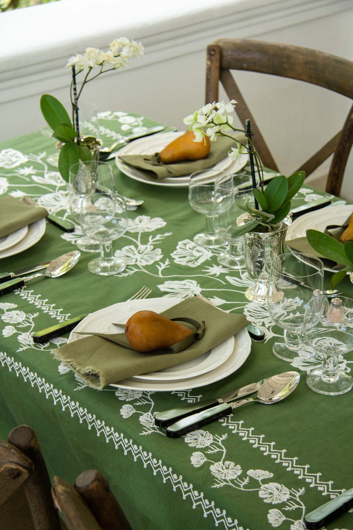 Close-up of Cosmo Rectangular Tablecloth in Green showcasing white floral embroidery and geometric border with a formal table setting