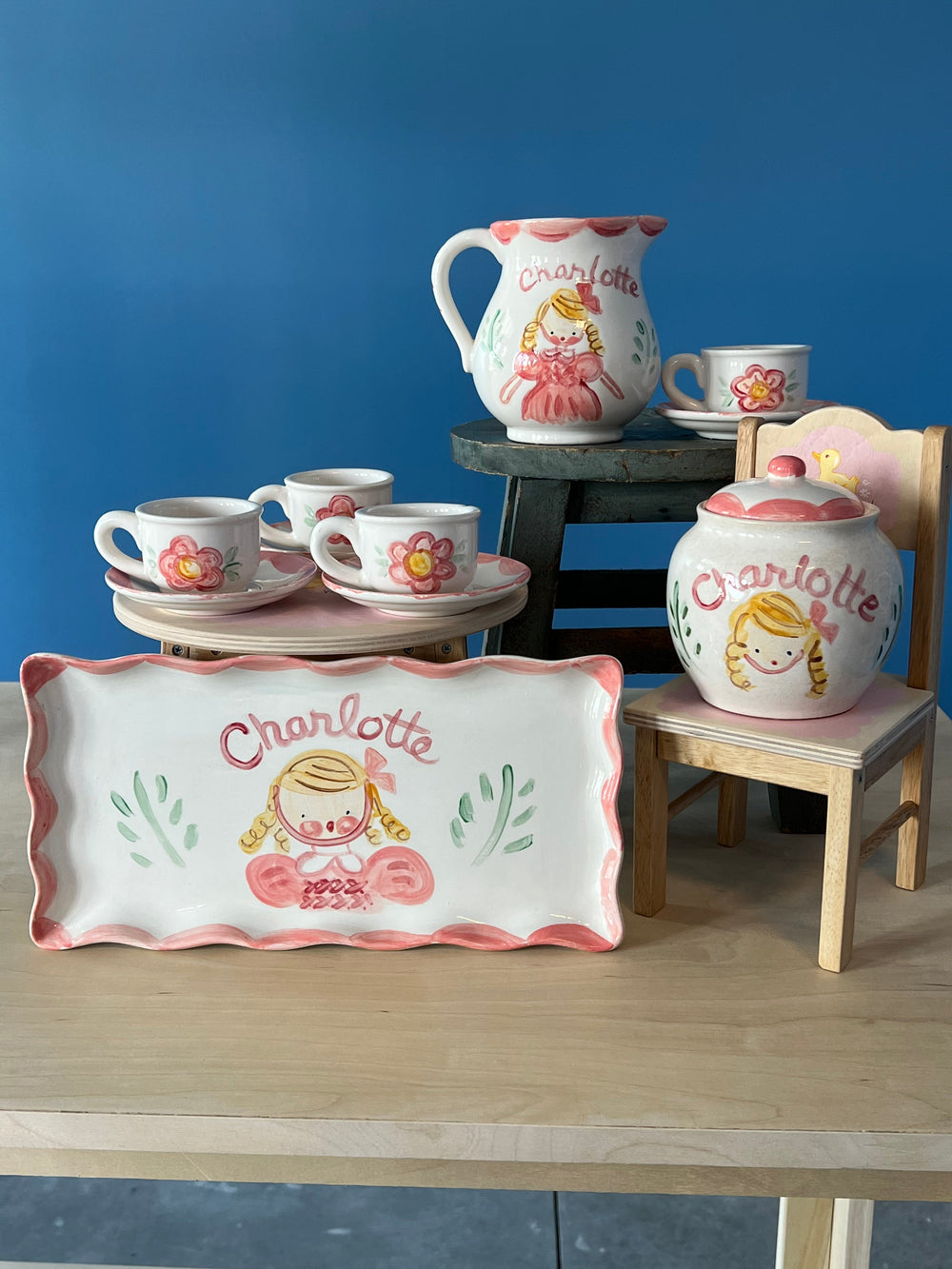 Front view of ceramic children’s tea set showcasing hand-painted pink flowers and the name Charlotte against a blue background