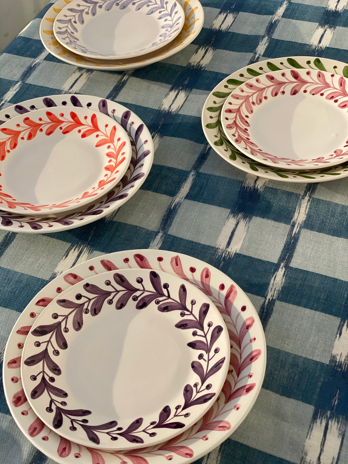 Close-up of Anna Rose Dessert Plate showcasing hand-painted red trim with stacked plates on a blue plaid textile background