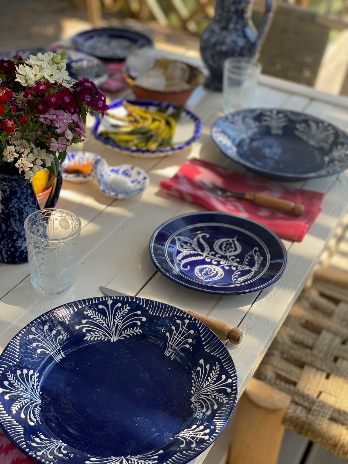 Close-up of Cobalt Tulip Dessert Plate showcasing its hand-painted floral pattern with other tableware in the background