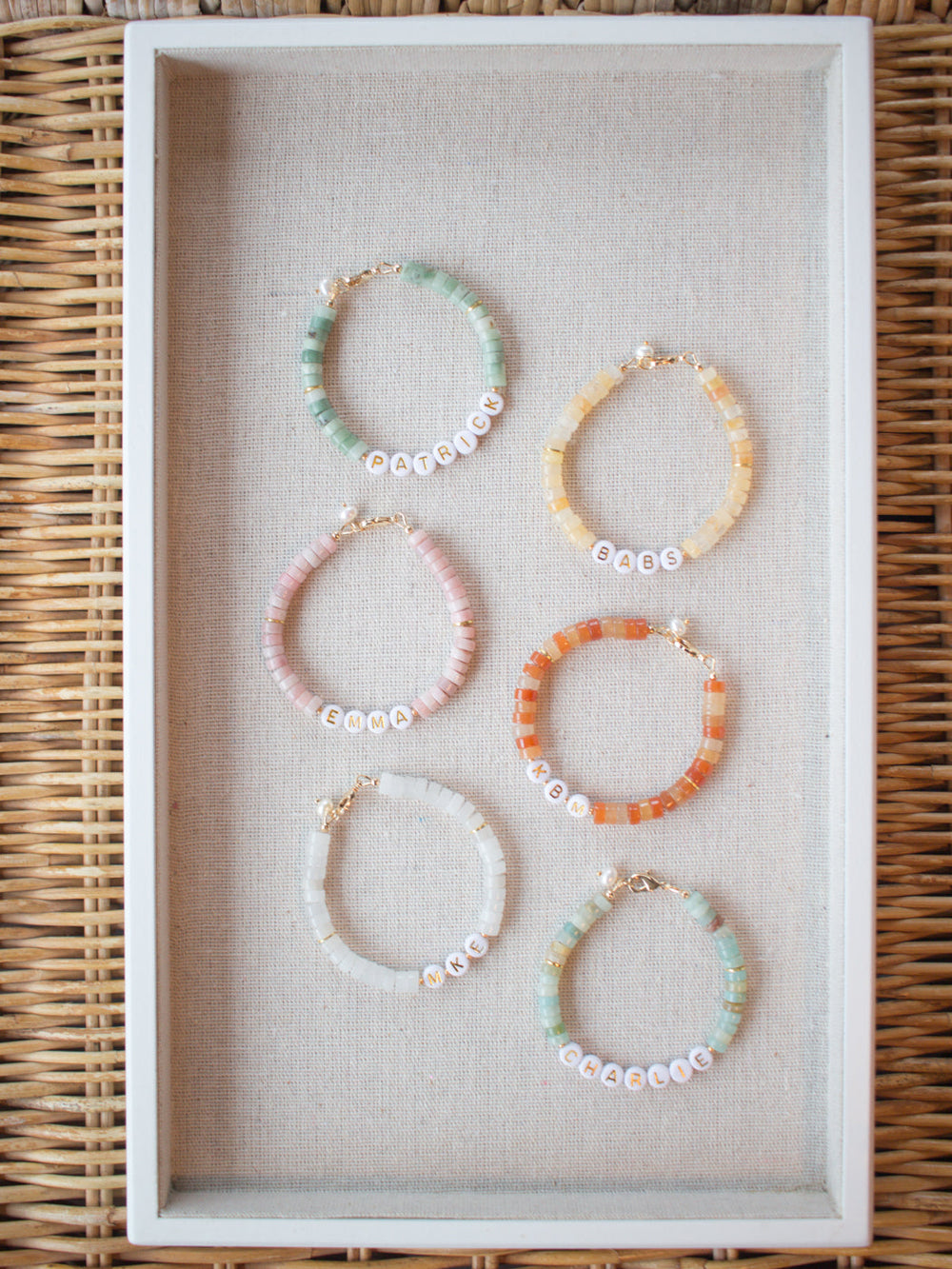 Top-down view of Tilly custom beaded bracelets with pastel and orange disc beads and white letter-name beads on a linen tray