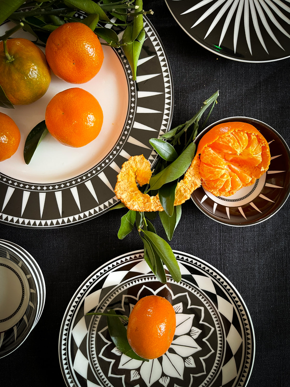 Marrakech patterned dinnerware arranged with oranges and greenery on a black table