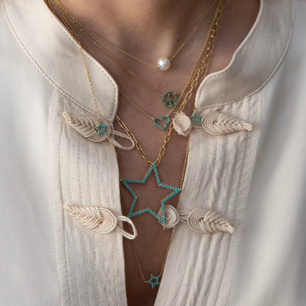 Pearl pendant necklace layered with gold chains and turquoise star charms on a model wearing a cream embroidered blouse