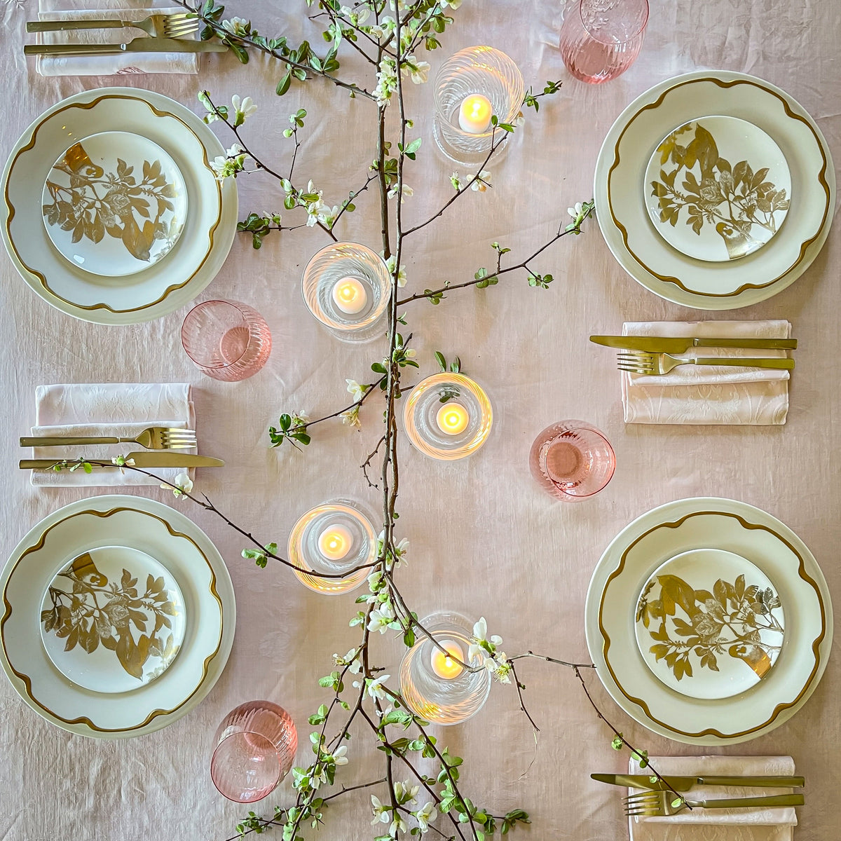 Bird's eye view of a spring tabletop featuring Caskata's Gold Arbor canapé plates on Grace Gold buffet plates around an assortment of Quinn mouth-blown glassware and a flowering branch centerpiece. 