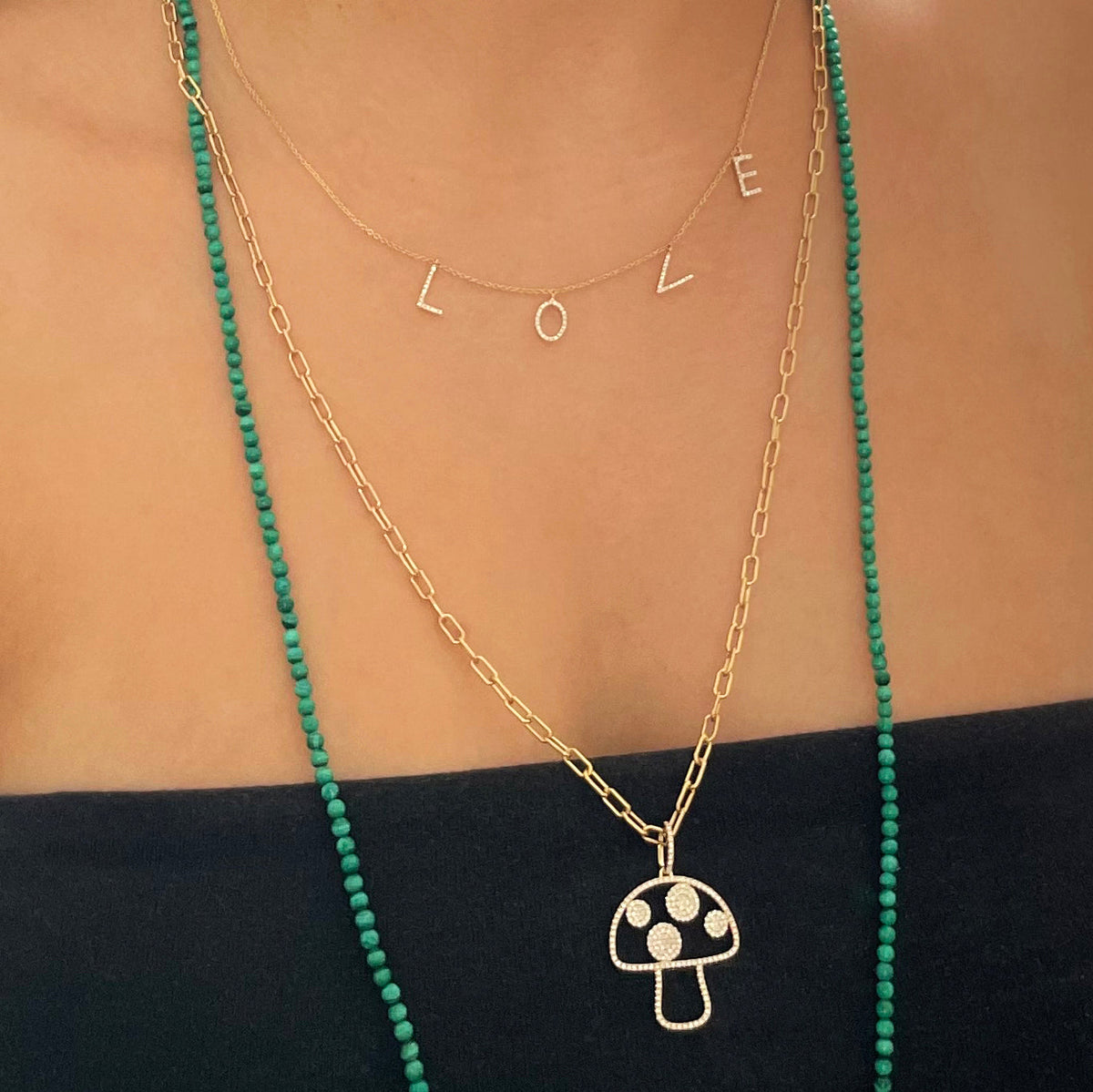 Close-up of Separated Love Text Necklace showcasing a gold chain with diamond-studded letter charms spelling LOVE, layered on a model wearing a black top