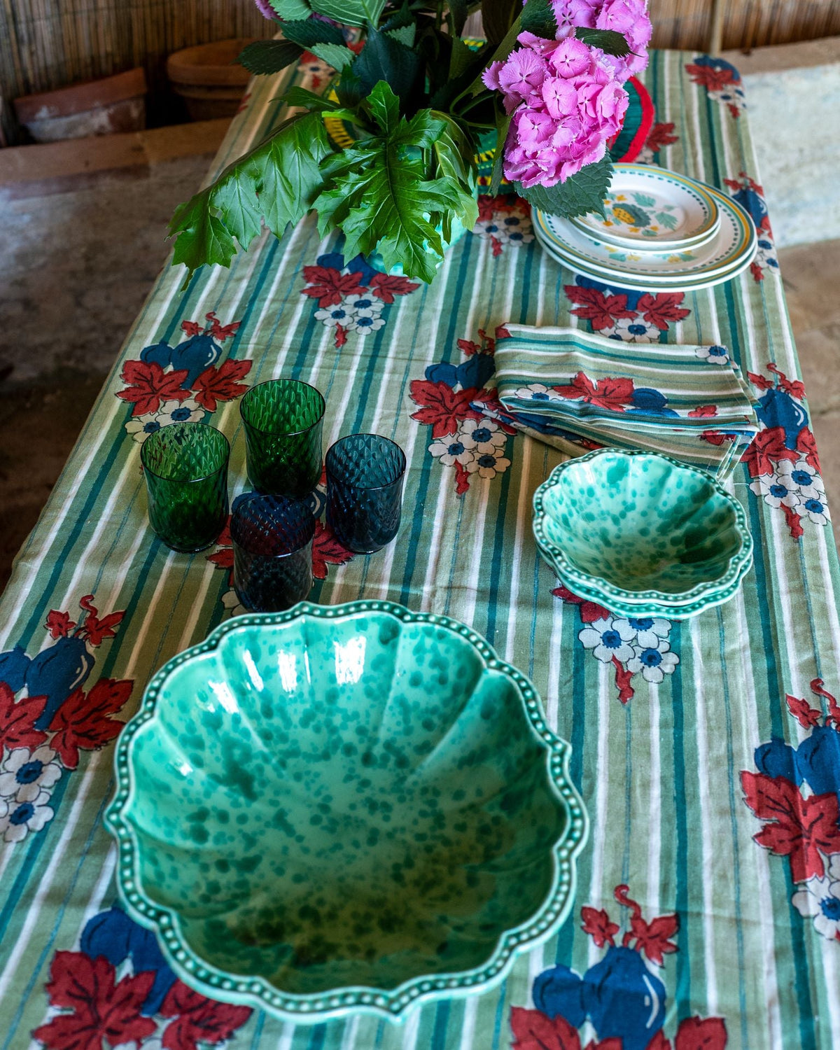 Overhead view of Speckled Serving Bowl in Green showcasing its scalloped rim and speckled ceramic on a floral tablecloth