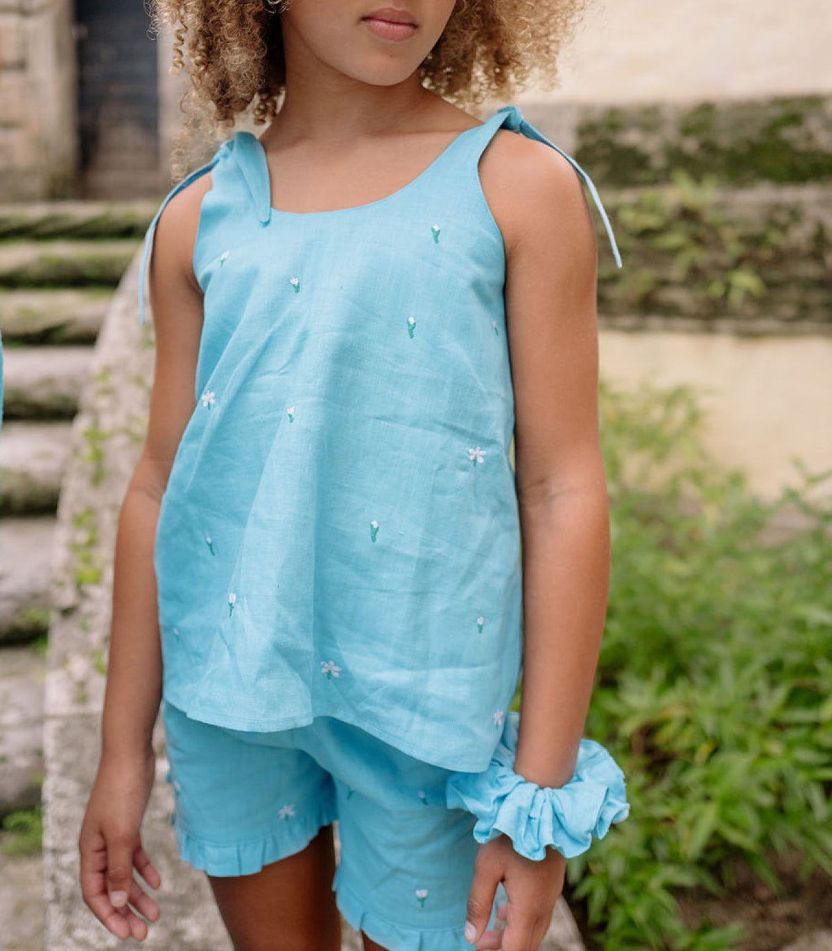 Front view of minnow x Fanm Mon Girls Lagoon Tie Knot Short Set with hibiscus embroidery and ruffle trim outdoors