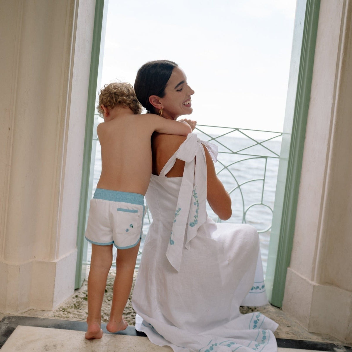 Back view of boys Coconut Grove white boardie showing turquoise elastic waistband and embroidered back pocket at seaside