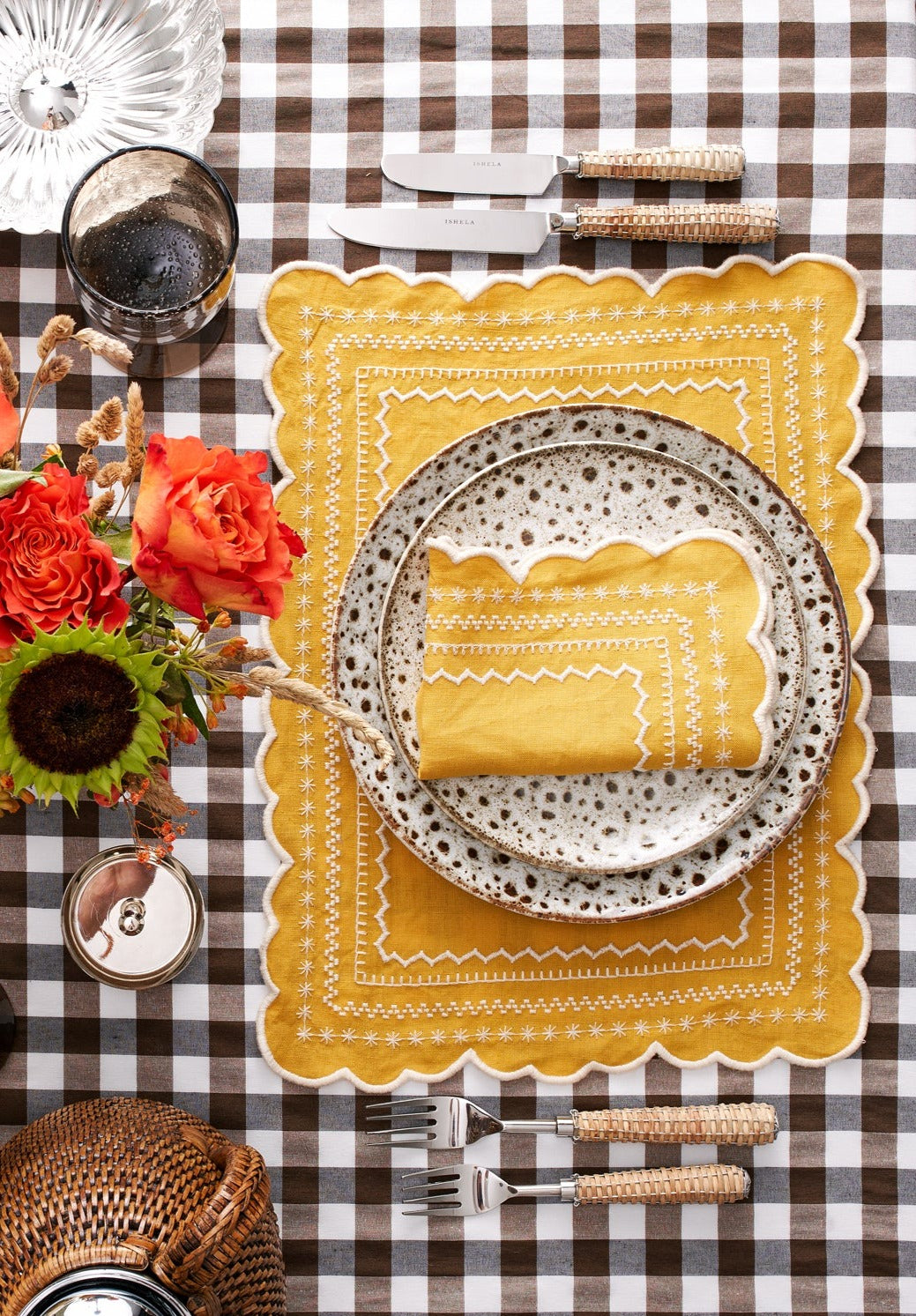 Top view of Isabelle placemat in mustard with scalloped edges and white embroidered trim on brown gingham table