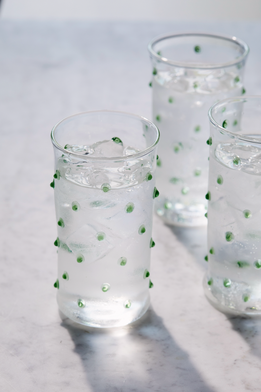 Front view of Pom highball glass showcasing raised green bobbles and ice, set on a marble tabletop