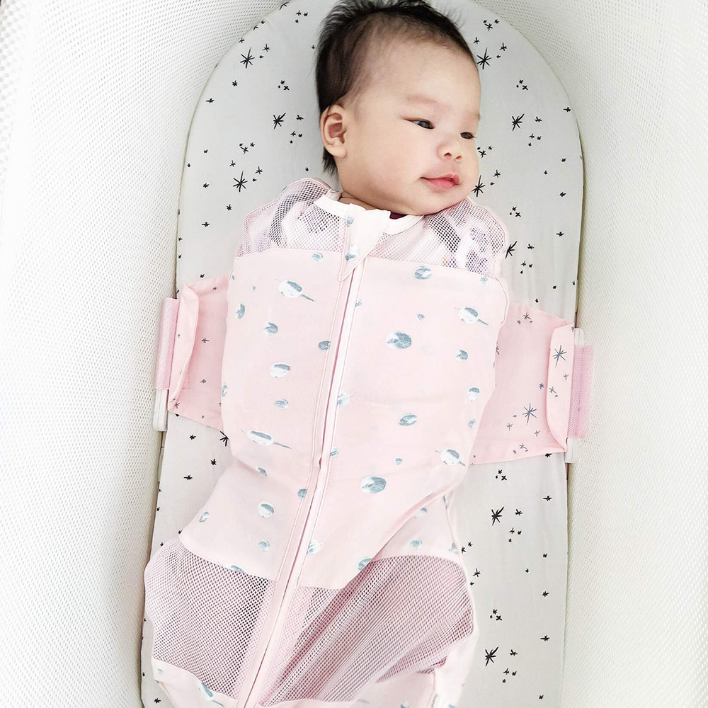 Top-down view of pink SNOO Sleep Sack showing silver planet print, mesh leg panels, front zipper, and swaddle wings in a white bassinet