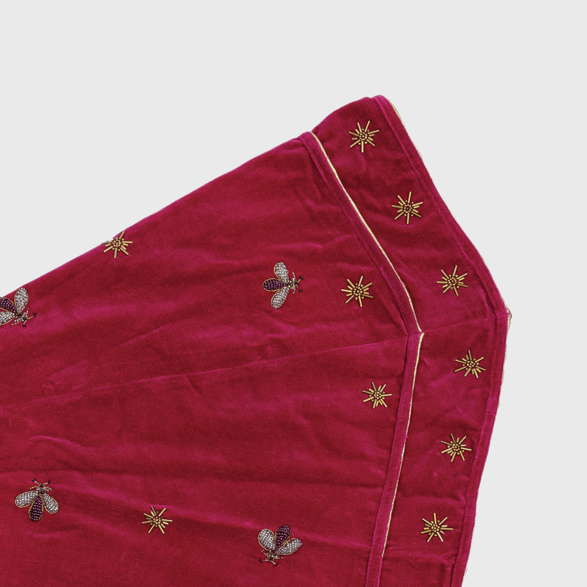Close-up of Sparkle Bee Tree Skirt in Berry showcasing cotton velvet with hand-embroidered glass beads against a light gray background