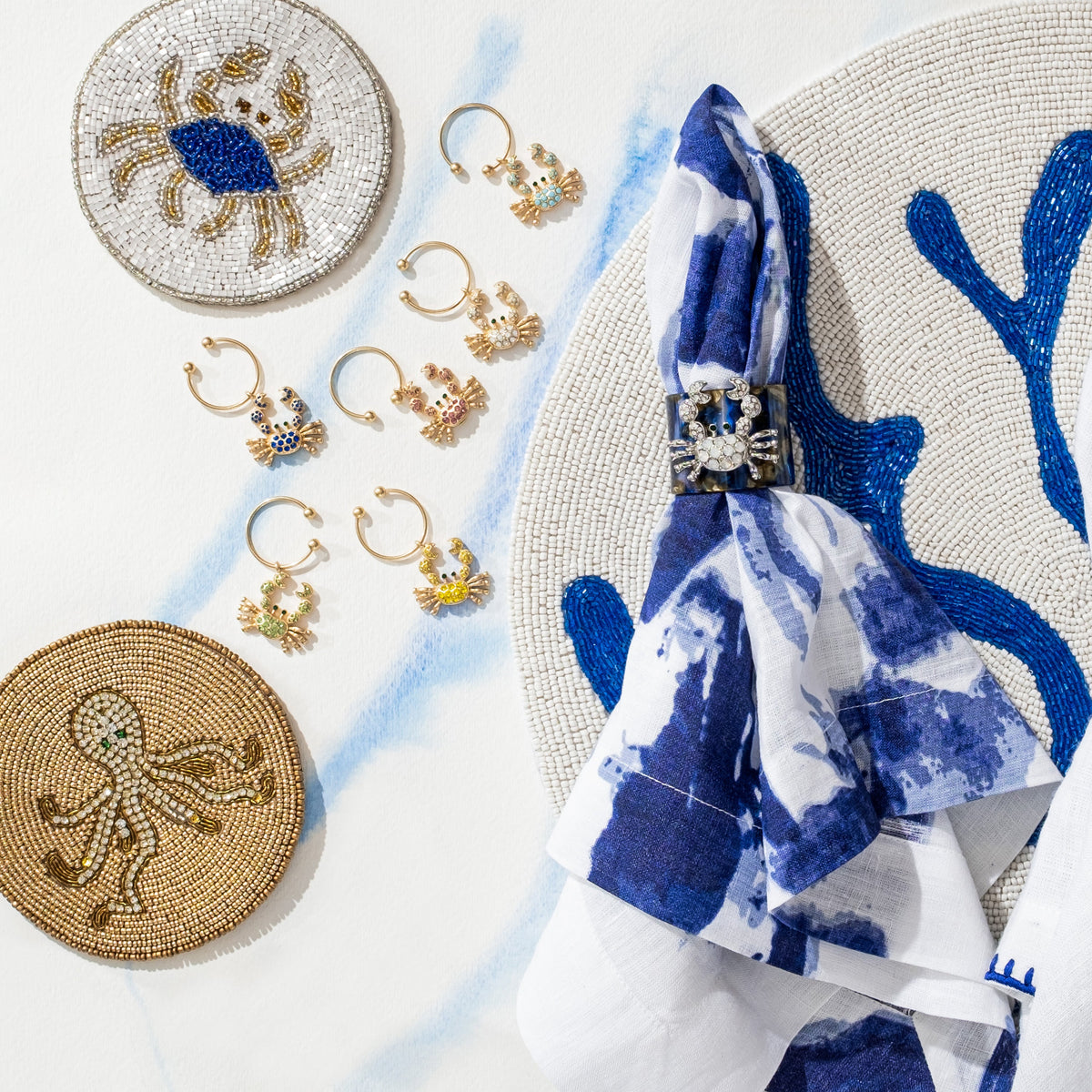 Top view of Coral Hand Beaded Placemat in Cobalt showcasing blue coral motifs with jewelry and a blue napkin