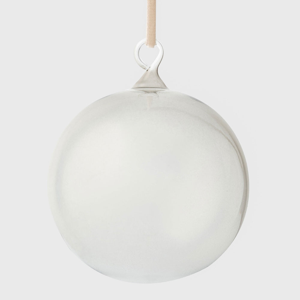 Front close-up of clear glass bubble ornament showing smooth hand-blown sphere with loop and beige ribbon on gray background