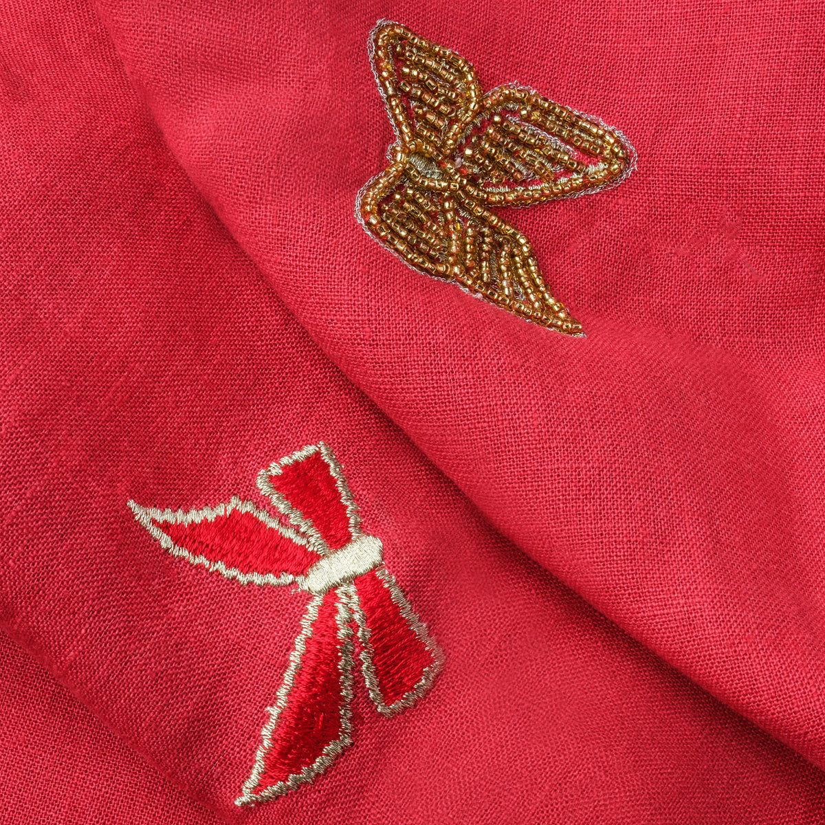 Close-up of Bow Extra Large table runner showing red linen with embroidered bows and a gold-beaded bow