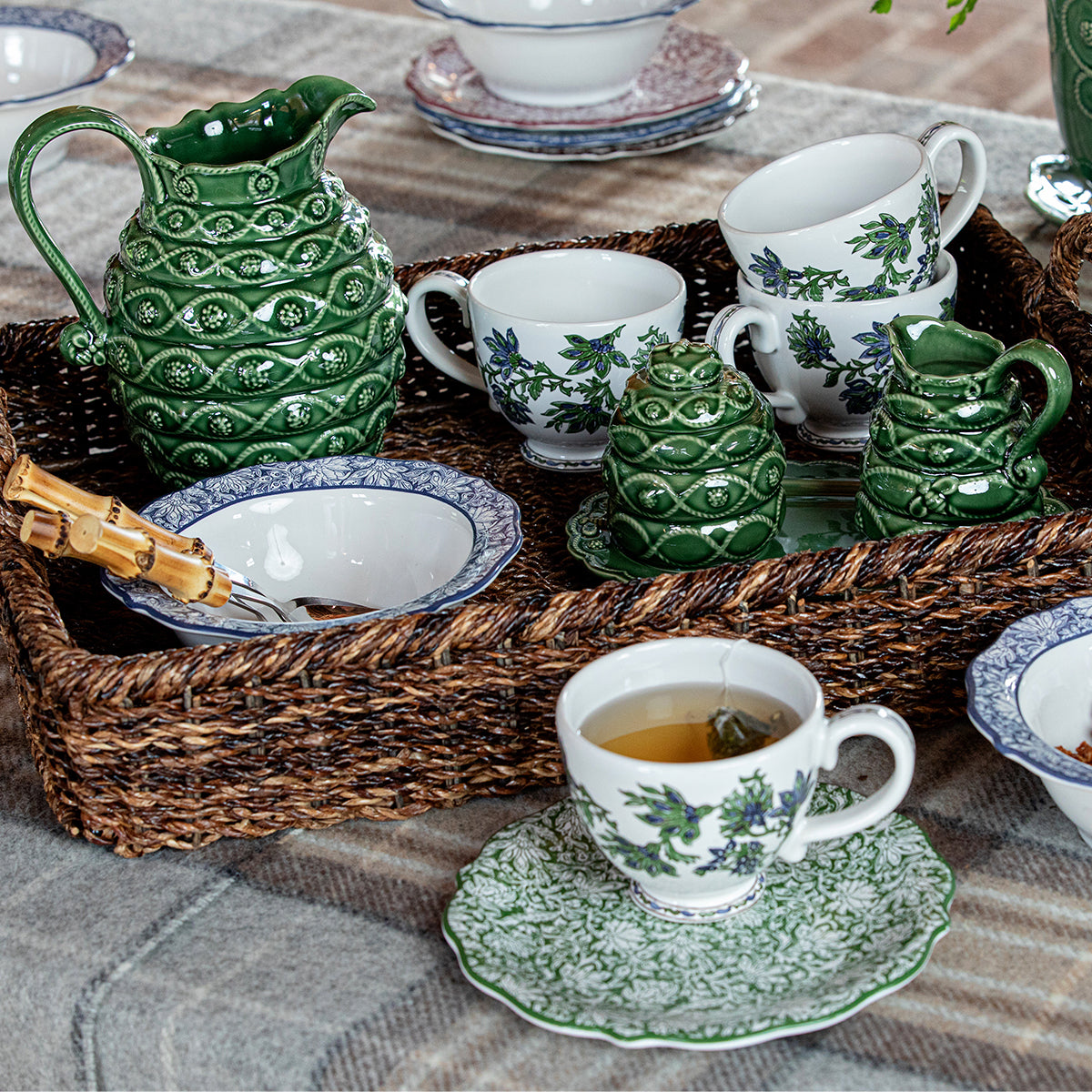 Green glazed creamer and sugar set displayed on a woven tray among floral tableware