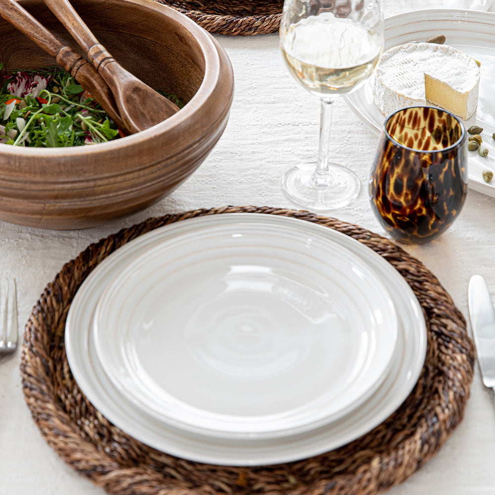 Top down view of Bilbao Whitewash dessert salad plate showing whitewash concentric rings and hand hewn texture on a woven charger