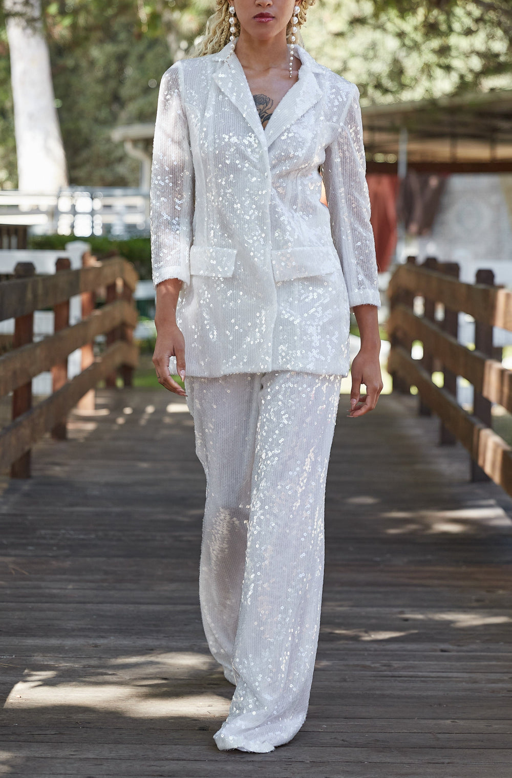 Front view of Katharine Suit in Sequin showing white sequin blazer and wide-leg pants on a model on a wooden bridge