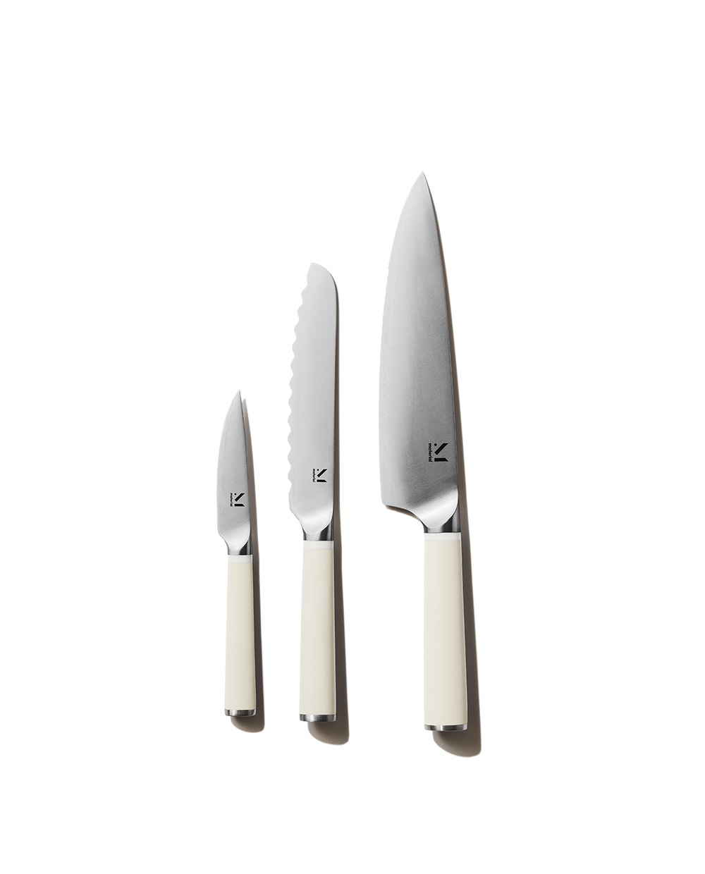 Front view of The Trio of Knives showing chef, serrated, and paring blades with cool neutral cream handles on white