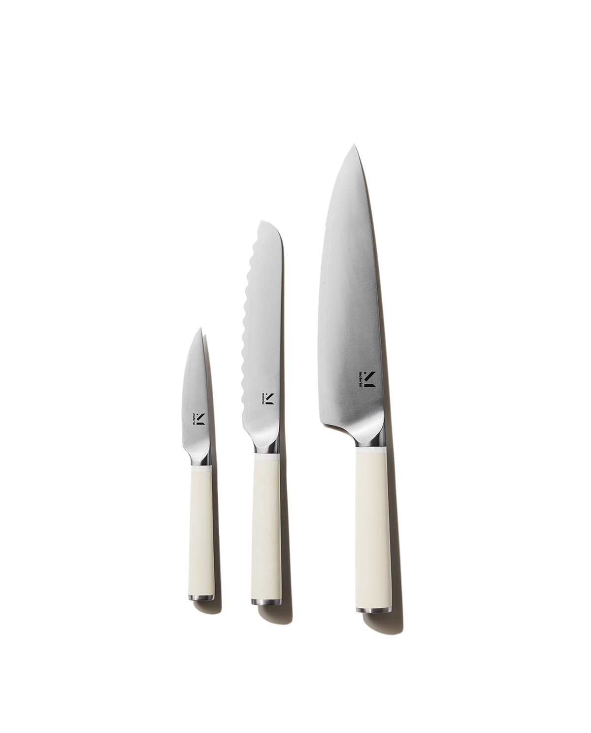 Front view of The Trio of Knives showing chef, serrated, and paring blades with cool neutral cream handles on white