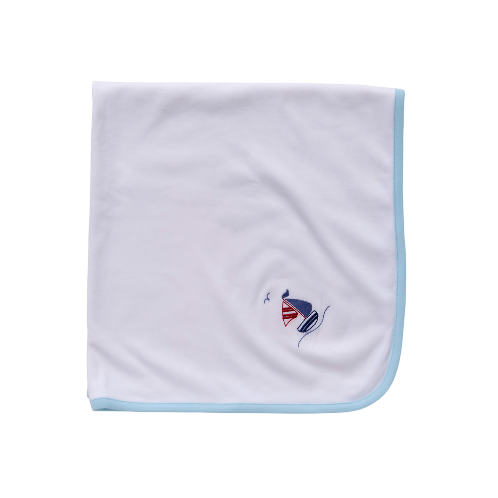 Flat lay of baby blanket showcasing light blue binding and small embroidered sailboat on white background