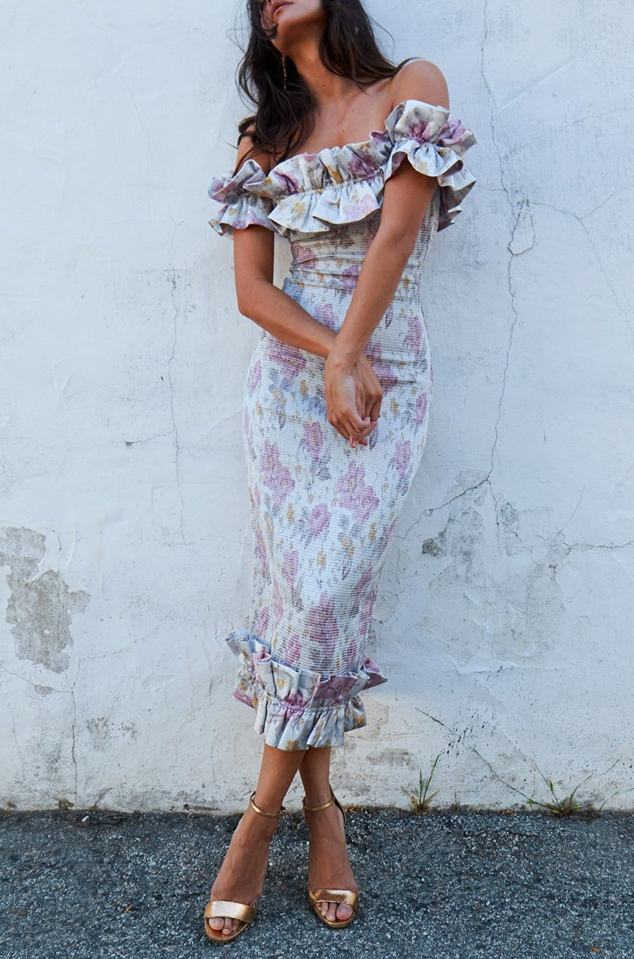 Full-length view of The Lilac Dress in Purple Floral showcasing ruffles and elastic ruching on a model against a pale wall