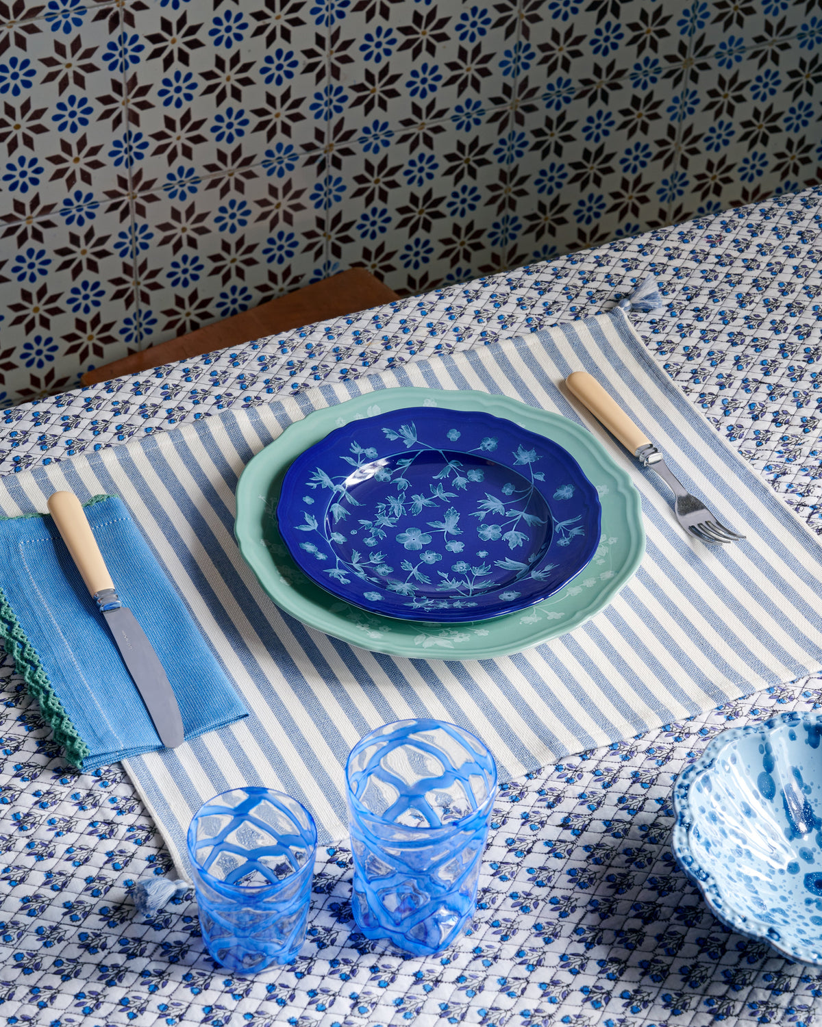 Light blue striped placemat styled on a table with floral plates, blue glasses, cutlery, and patterned linens