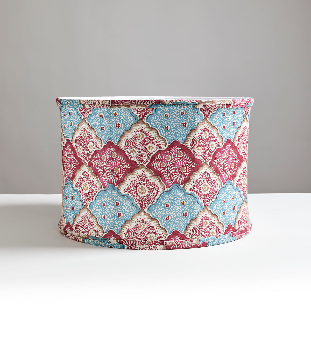Front view of Akira drum lampshade showcasing Peacock Rose and Porcelain Blue scalloped batik pattern on white tabletop background