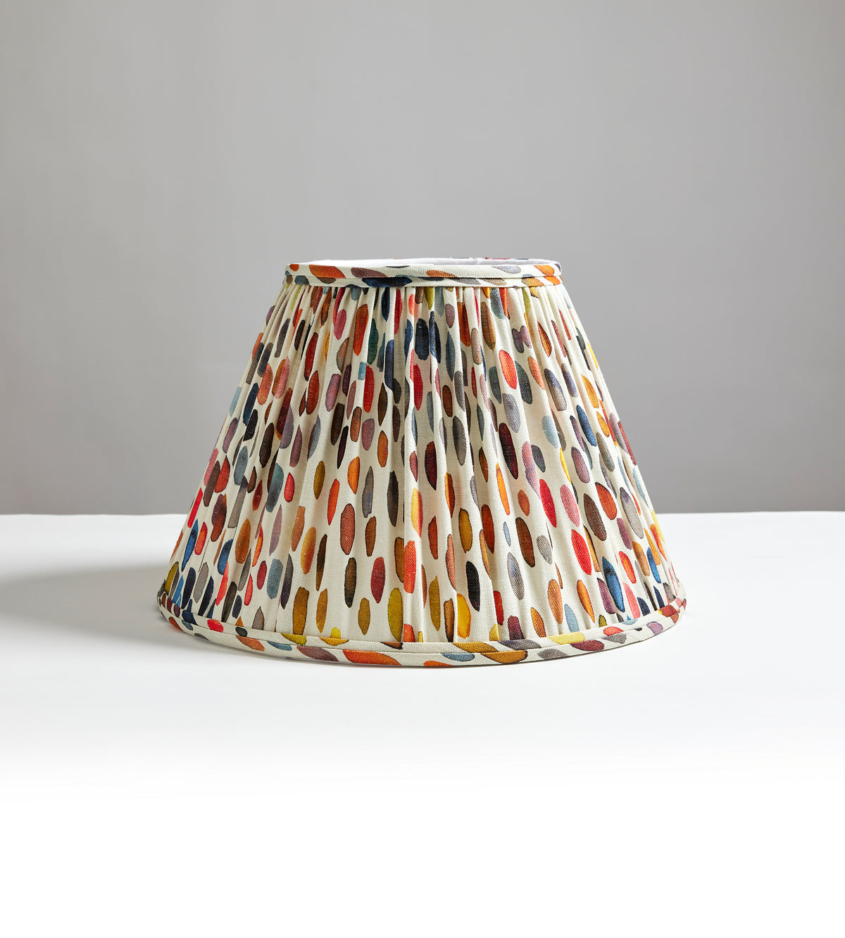 Front view of Jamboree Pleated Shade showcasing pleated cream fabric with multicolored brushstroke oval pattern on neutral gray background
