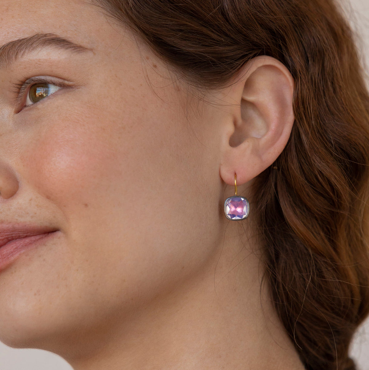 Close up of Luzia Button Earrings showcasing cushion cut lavender moon quartz and 14K gold ear wire on a model’s ear
