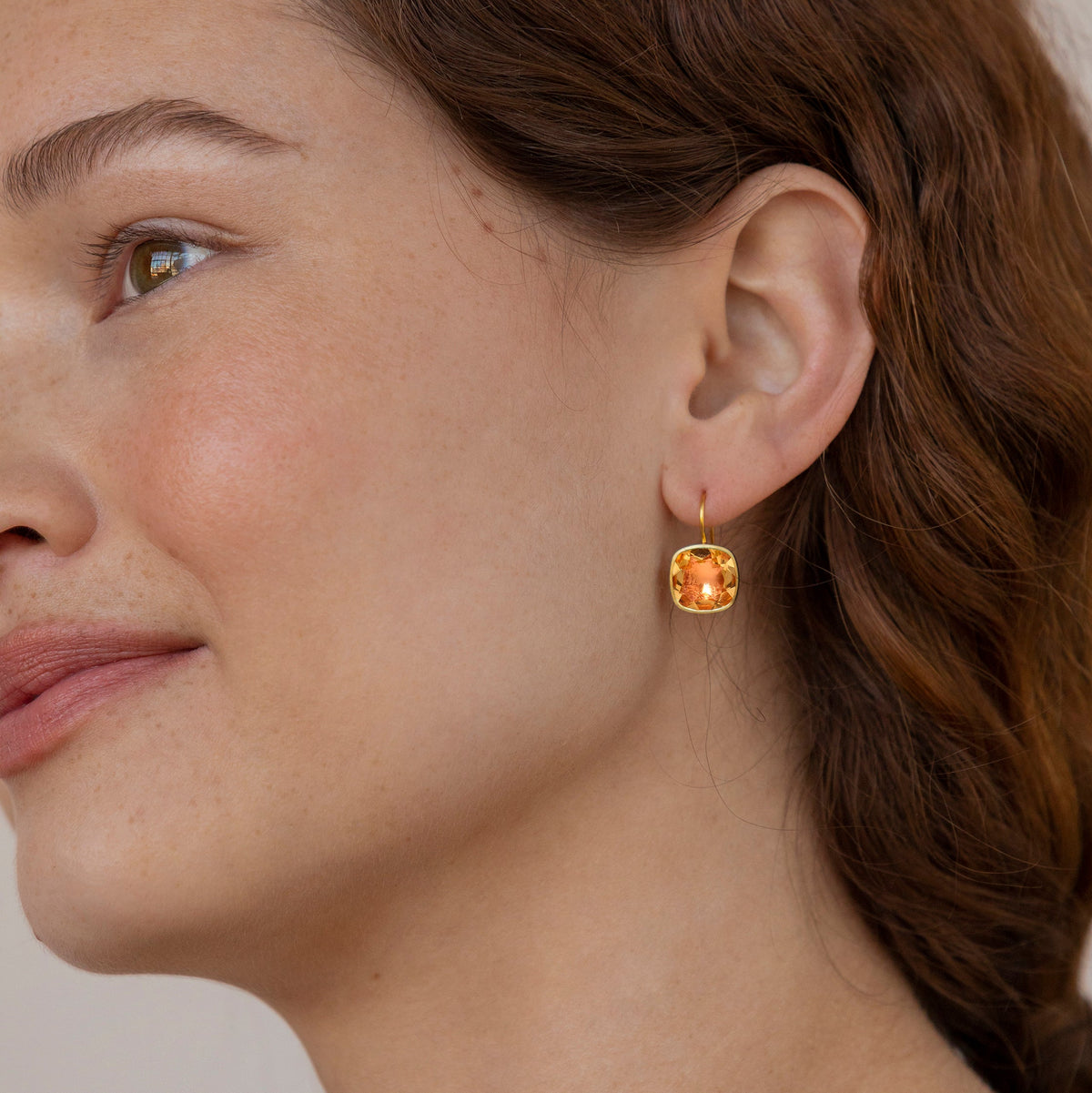 Close-up side view of Luzia Button Earrings showcasing cushion-cut foiled citrine in a smooth 14K yellow gold bezel on a model’s ear