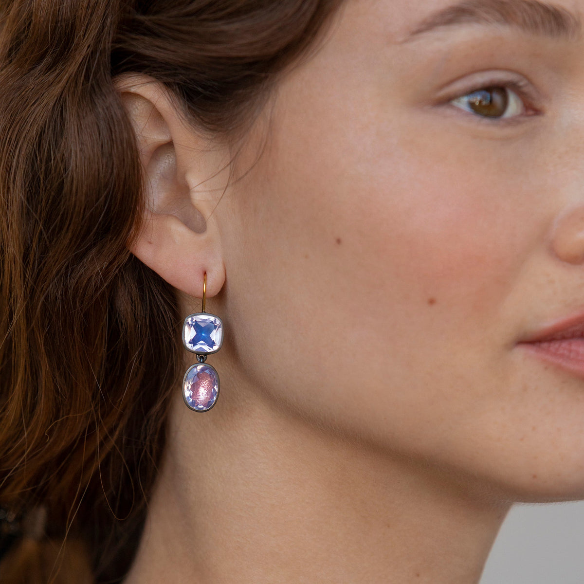 Close-up side view of Luzia Cushion Oval Double Drop Earrings showcasing two lavender moon quartz stones in smooth bezel settings on a model’s ear
