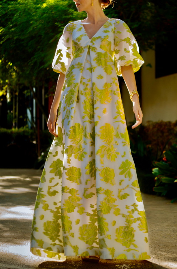 Front view of Full Sleeve Pleat Front Gown showcasing puffed full sleeves, center front pleat, and pistachio-gold floral organza in a sunlit garden