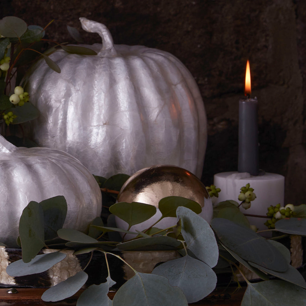 Front view of large Capiz pumpkin in pearl showing hand‑pieced iridescent shell with eucalyptus, gold sphere, and lit candle