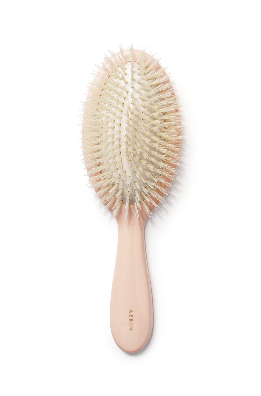 Top view of AERIN large pink hairbrush with mixed boar and nylon bristles and gold logo on acrylic handle