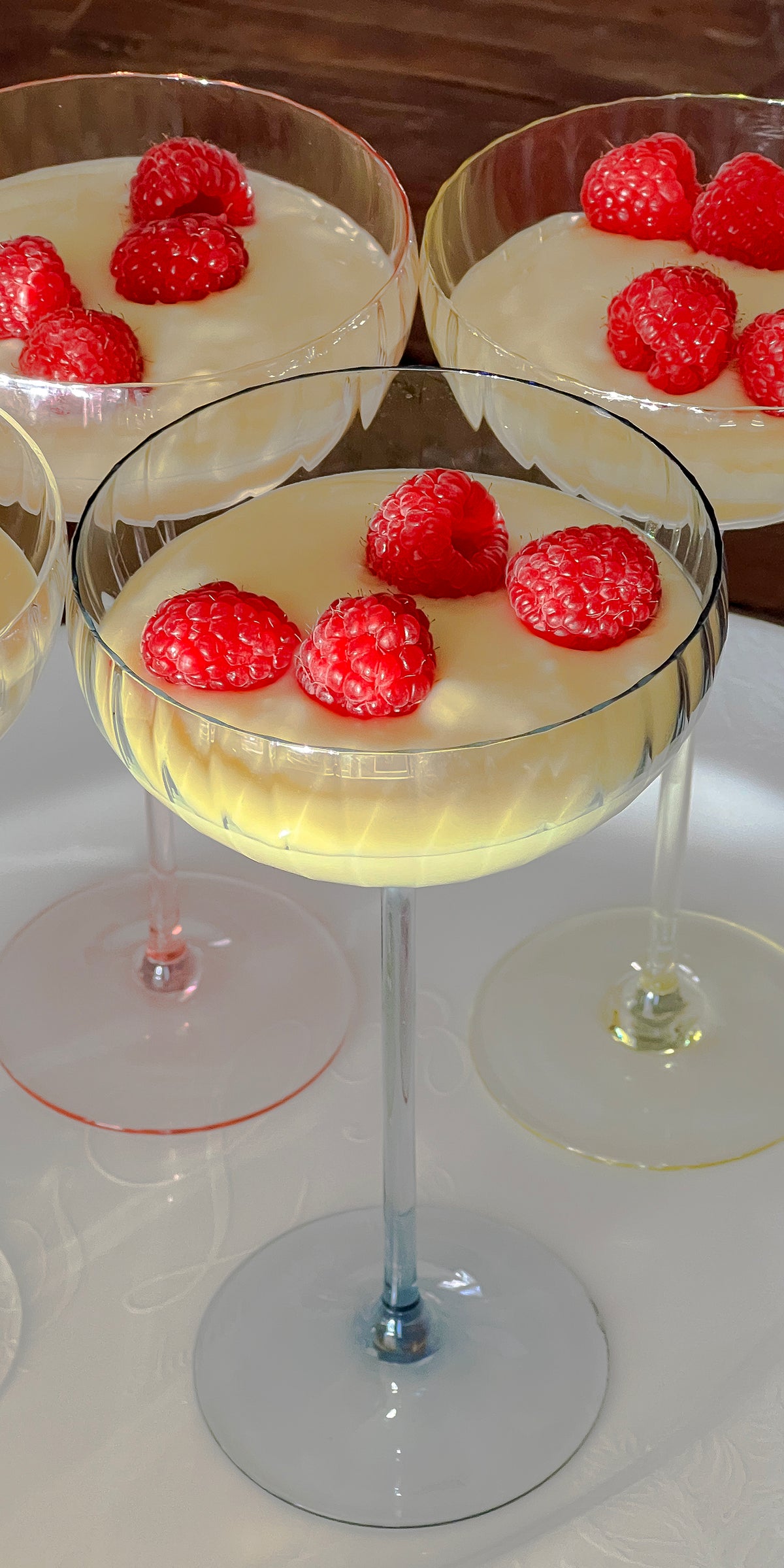 Quinn Citrine coupe glasses hold lemon pudding topped with raspberries on a table