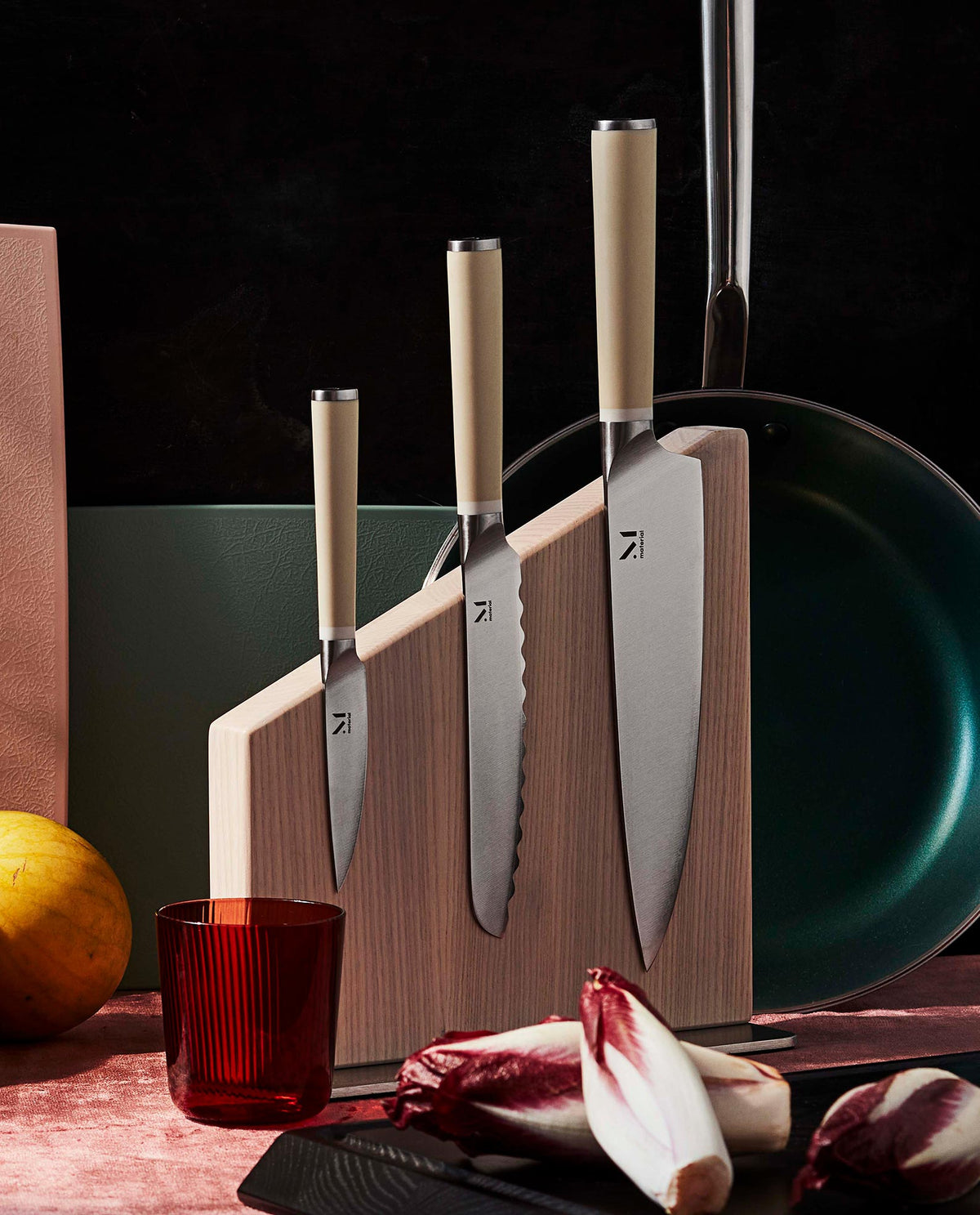 Front view of The Knives + Stand showcasing three knives in a walnut magnetic stand with kitchen props