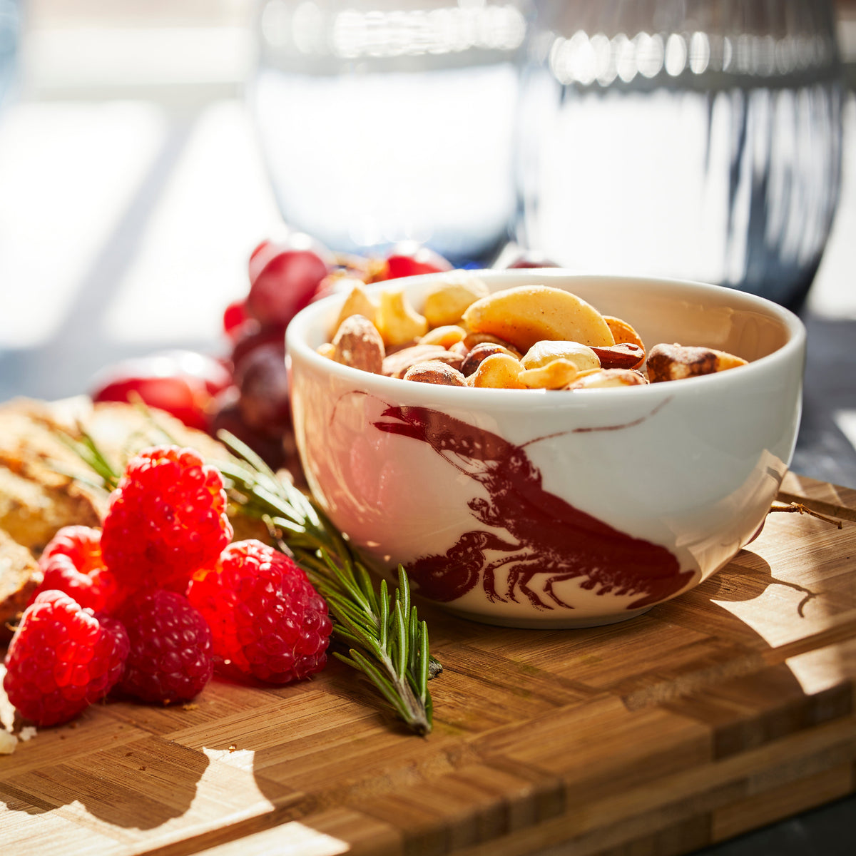 A Red Lobster Snack Bowl from Caskata holds nuts on a wooden charcuterie board.